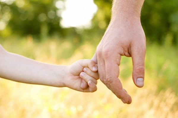 Ett barns hand håller om lillfingret på en vuxens hand mot en gulgrön bakgrund.