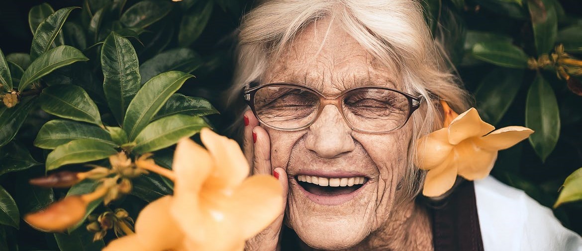 äldre kvinna som skrattar, omgiven av gula blommor