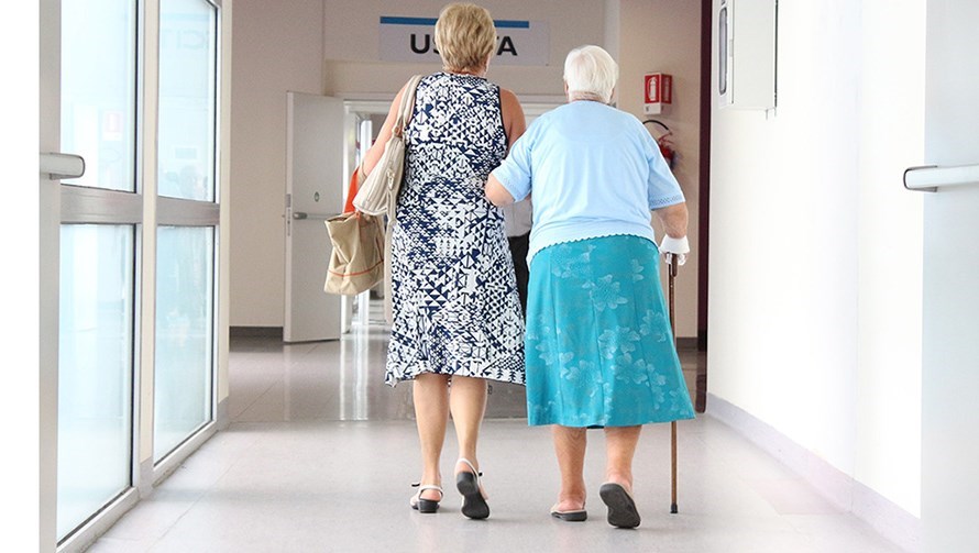 två kvinnor sedda bakifrån går i en sjukhuskorridor